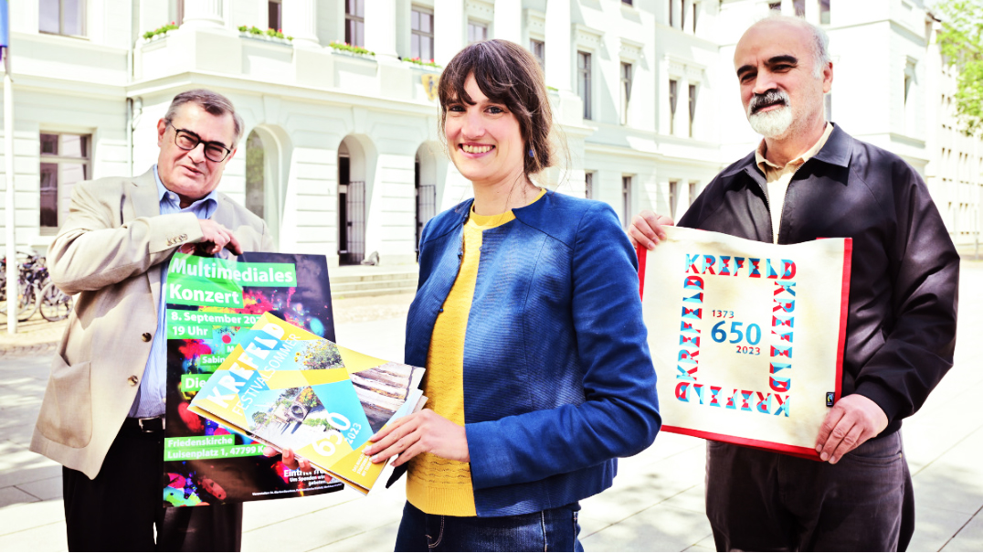 Claire Neidhardt, Leiterin des Stadtmarketings, präsentiert die neue Ausgabe des Jubiläumsmagazins. Günther Krenz von der Friedenskirche (l.) und Hayri Cakir vom Solidaritätshaus sind mit Bürgerprojekten vertreten.
